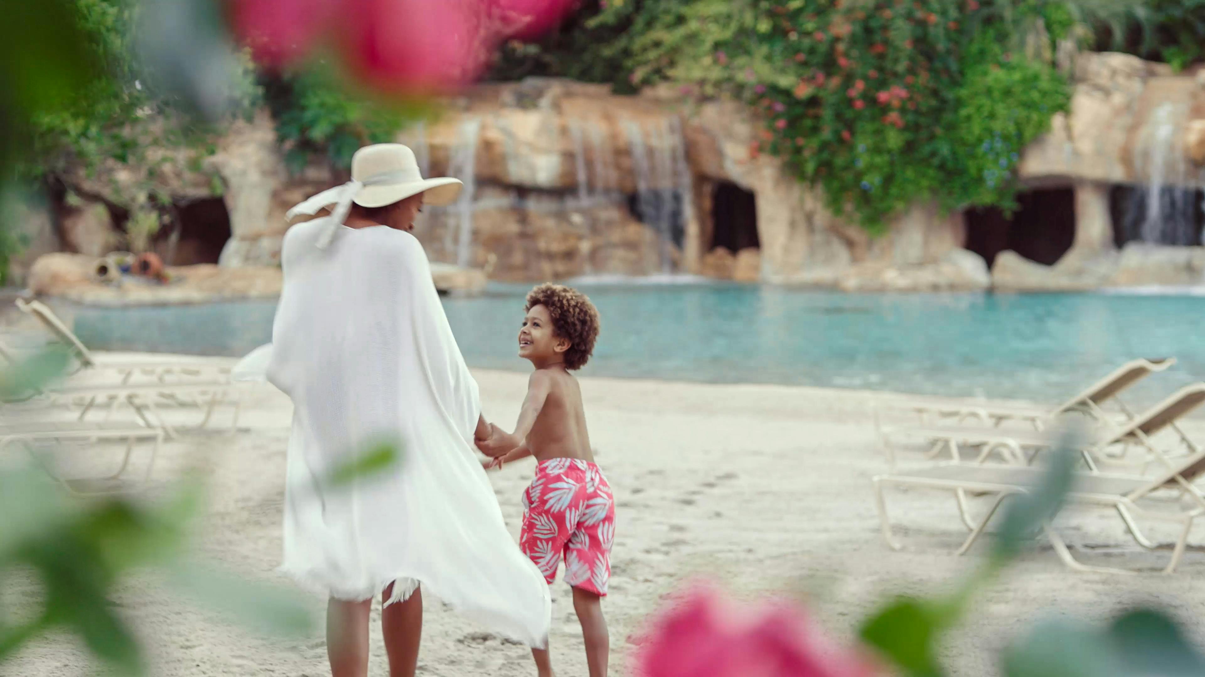 水着姿の大人と子供が、滝と緑豊かな砂浜に立っています。
