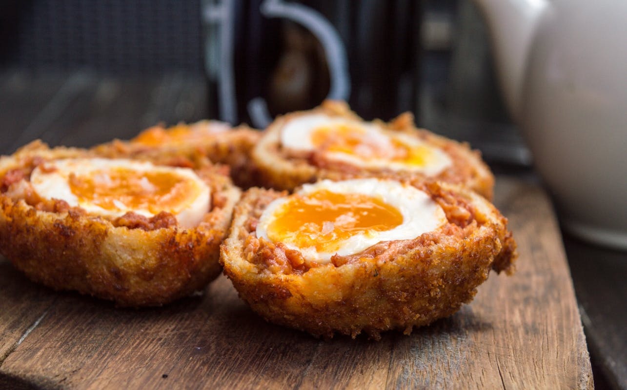 Close-up of four Scotch eggs with runny yolks on a wooden surface.