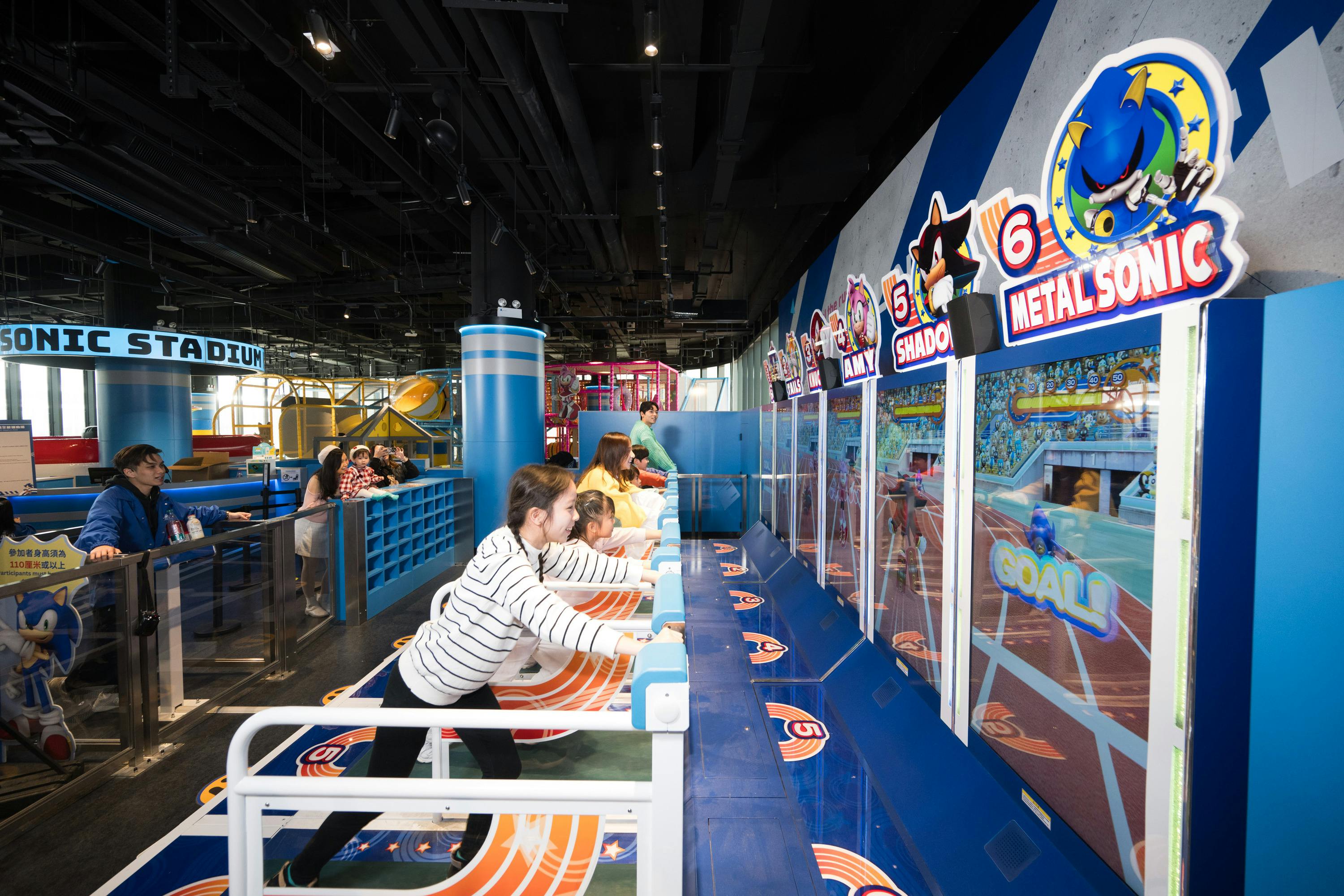 People playing arcade games in a brightly lit indoor amusement center featuring Sonic-themed decor and attractions.