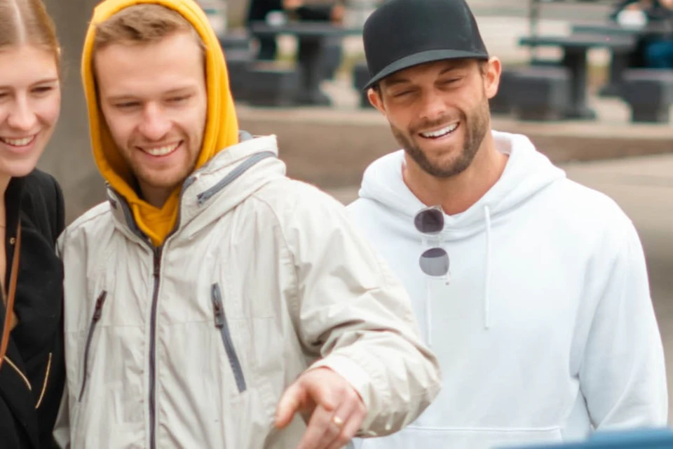 A group of people in casual clothing gathered outdoors, smiling and looking at a blue box held by a person in a blue jacket.
