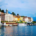 Colorful buildings and a dock with boats along a waterfront under a partly cloudy sky, with a tower visible in the background.