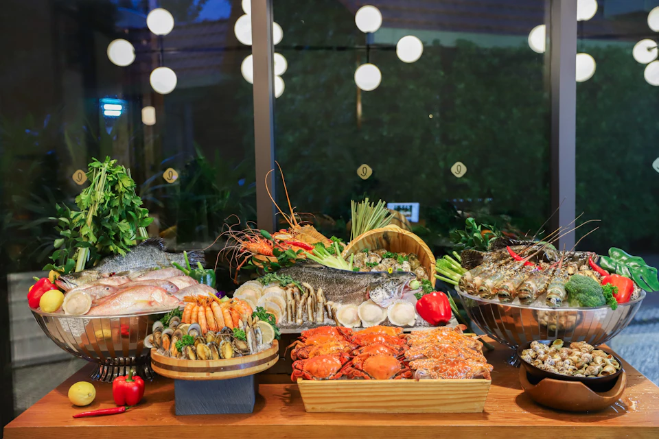 A buffet table displaying various fresh seafood, including crabs, prawns, fish, and shellfish, with vegetables and herbs.