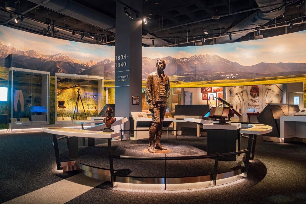 博物馆展览设有一个男人的青铜雕像、陈列桌、信息面板和背景中的一幅山壁画。