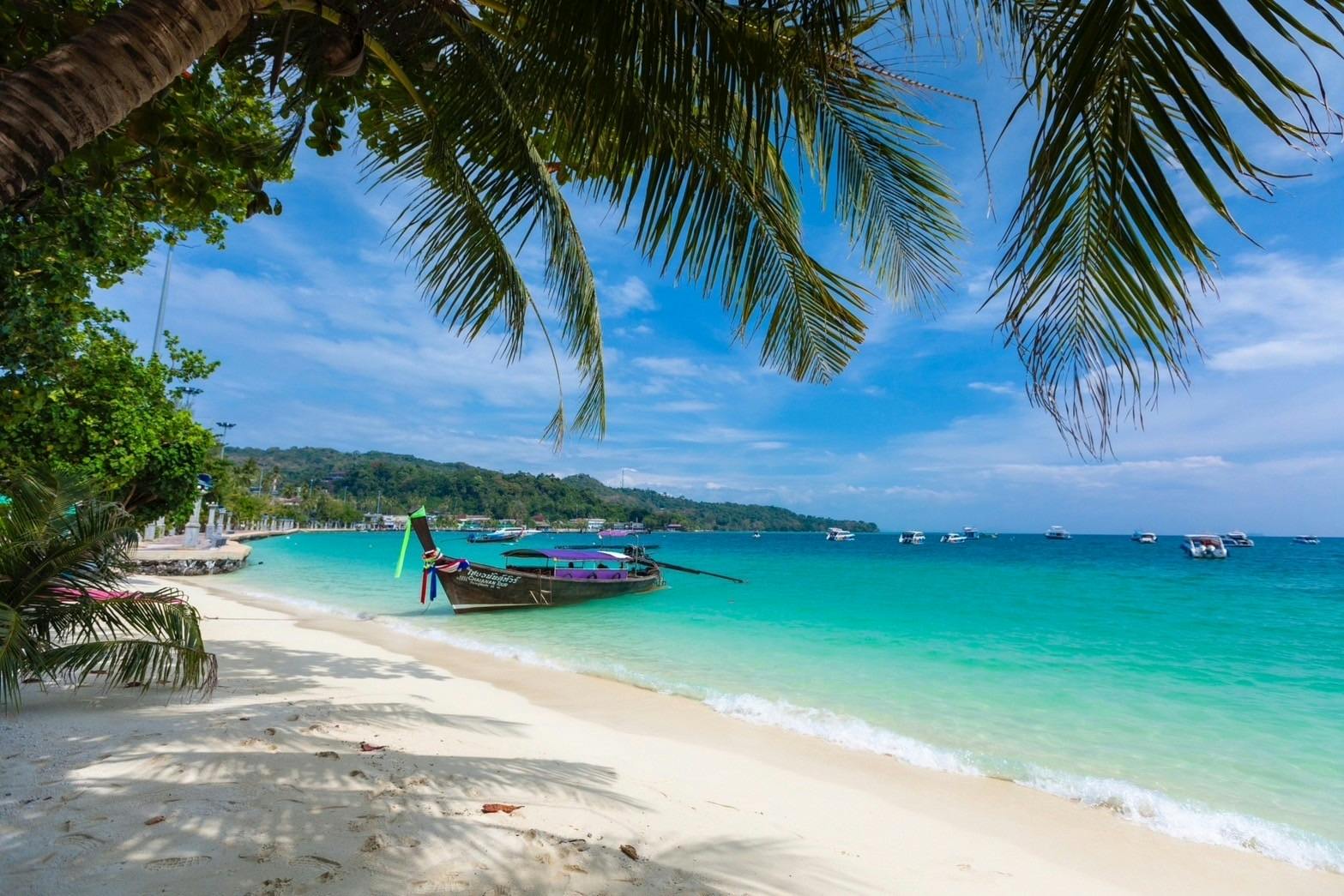 蓝天下的热带海滩，清澈的蓝色海水，传统的木船，棕榈树和远处的船只。