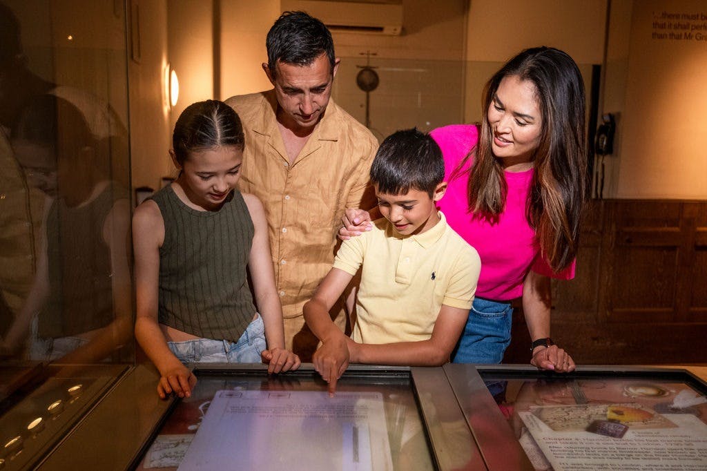 2 dorosłych i 2 dzieci patrzących na stolik wystawowy w muzeum lub sali wystawowej.