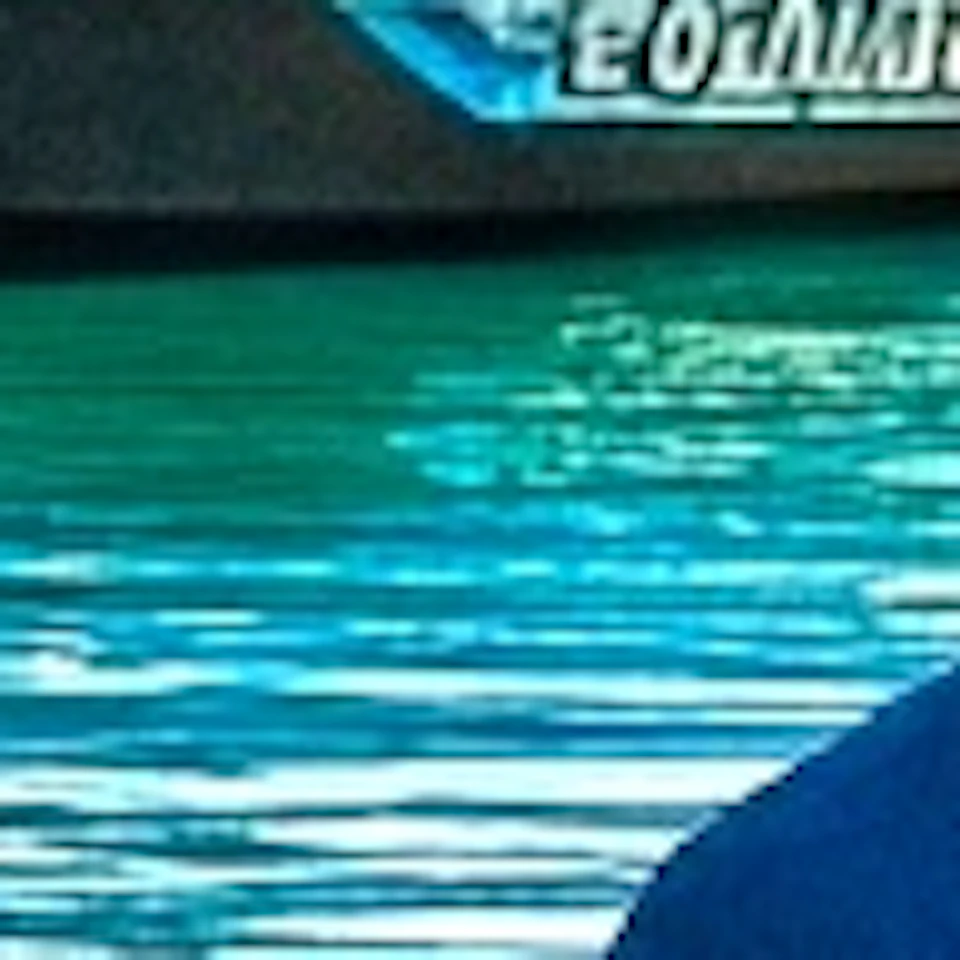 A group of people standing in shallow turquoise water holding drinks, with jet skis, palm trees, and a ship in the background.