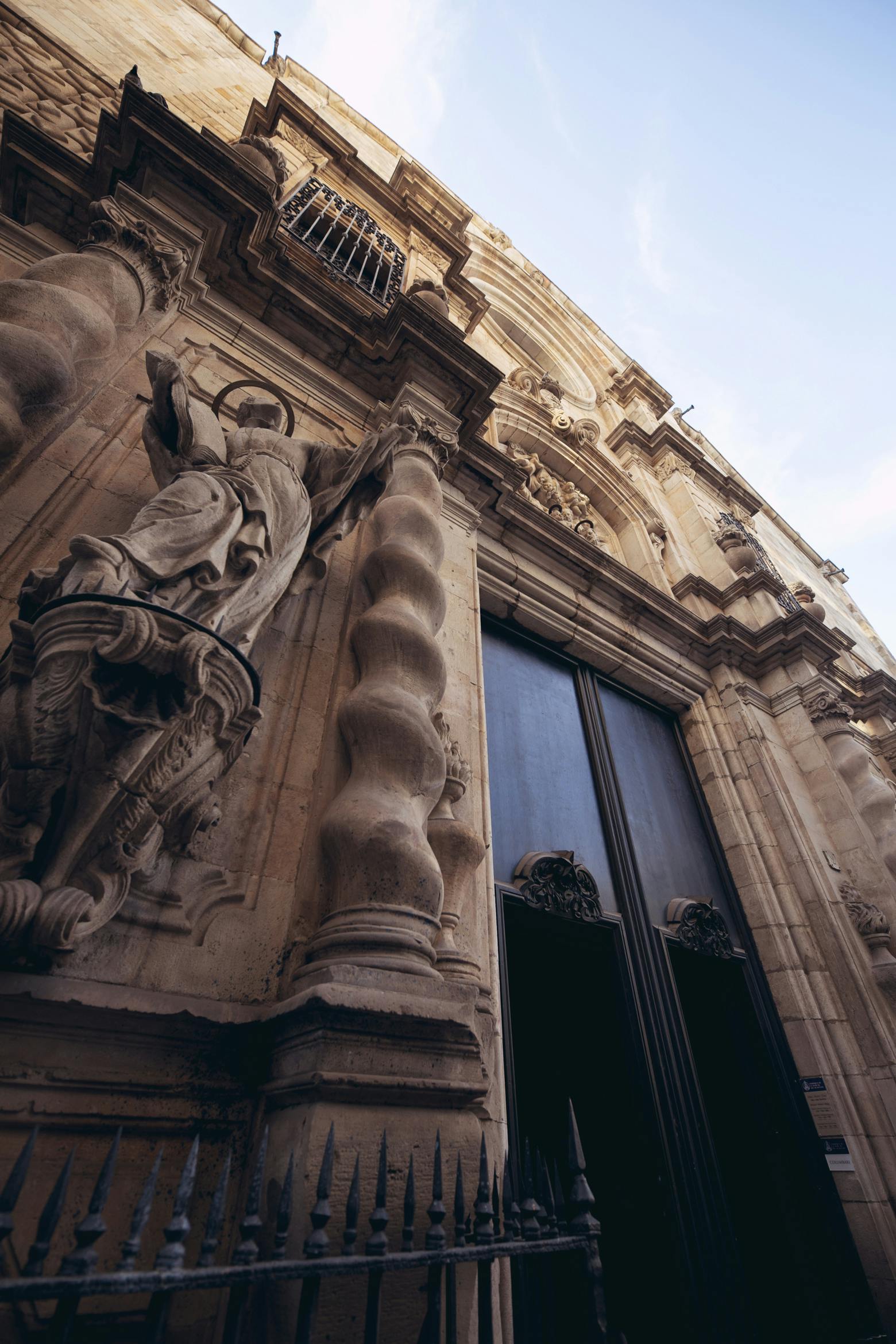 Façade en pierre ornée d'un bâtiment historique avec de grandes portes, des colonnes détaillées et une statue d'un personnage vêtu.