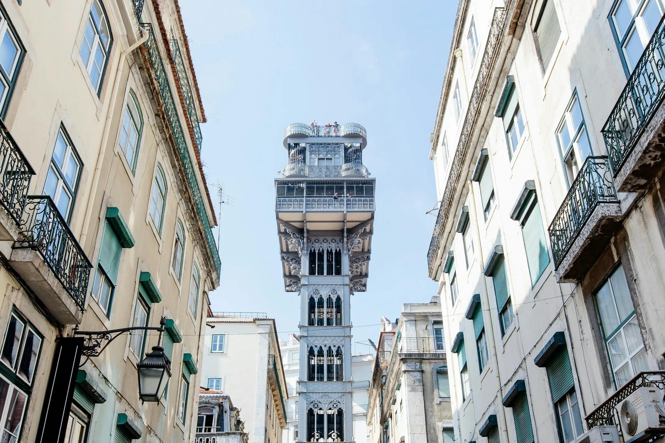 澄んだ青空の下、ベージュ色の建物と白い建物の間には、歴史的な鉄製のエレベータータワーが立っています。