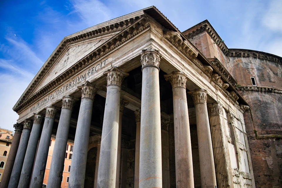 Ancient Roman temple with large columns and Latin inscription on the pediment, under a clear blue sky.