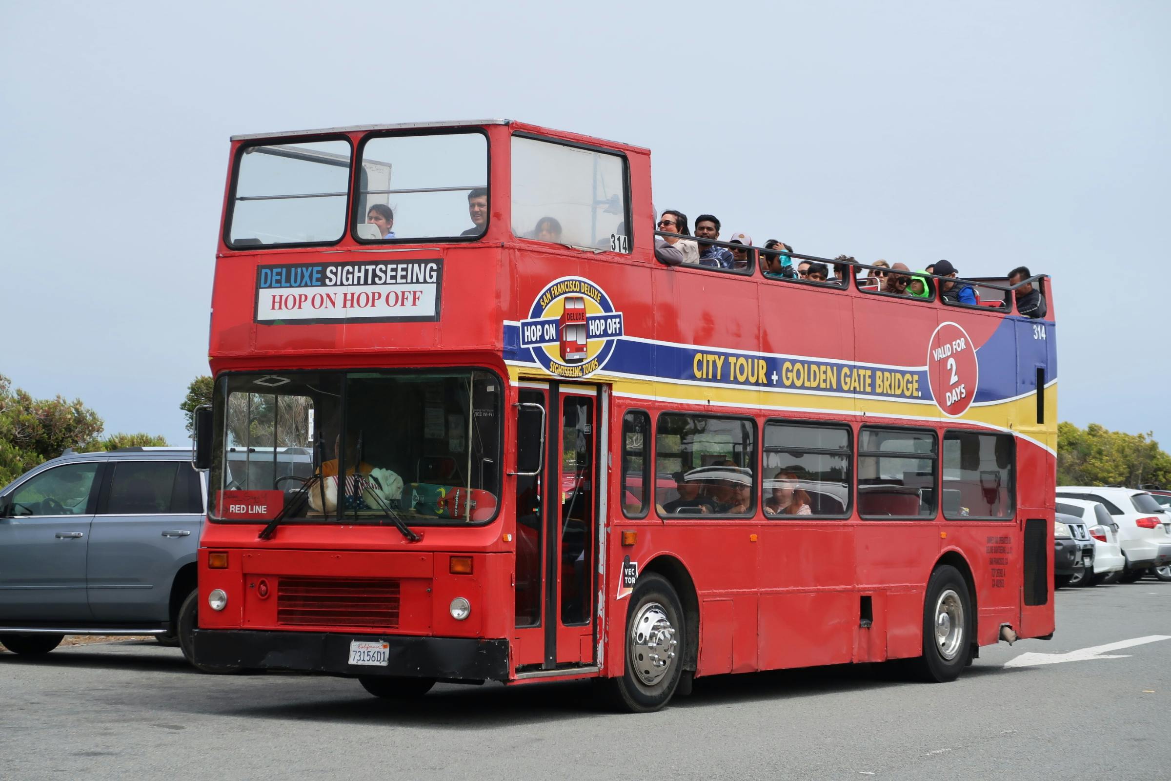 Bus touristique rouge à deux étages avec des passagers sur le pont supérieur, affichant des panneaux "City Tour + Golden Gate Bridge" et "Hop On Hop Off".