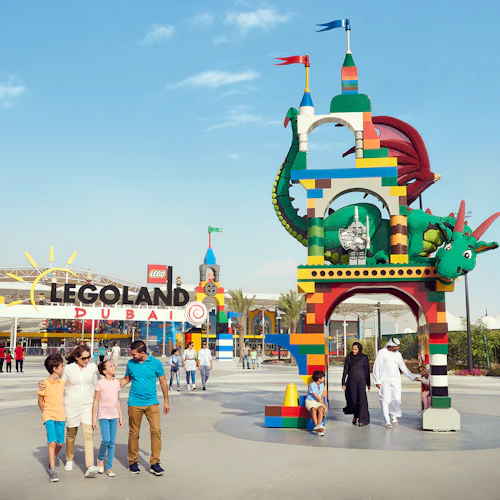 Familien spazieren in der Nähe des farbenfrohen Eingangs von LEGOLAND Dubai, der einen großen LEGO Drachen und einen lebhaften Torbogen unter einem klaren Himmel zeigt.
