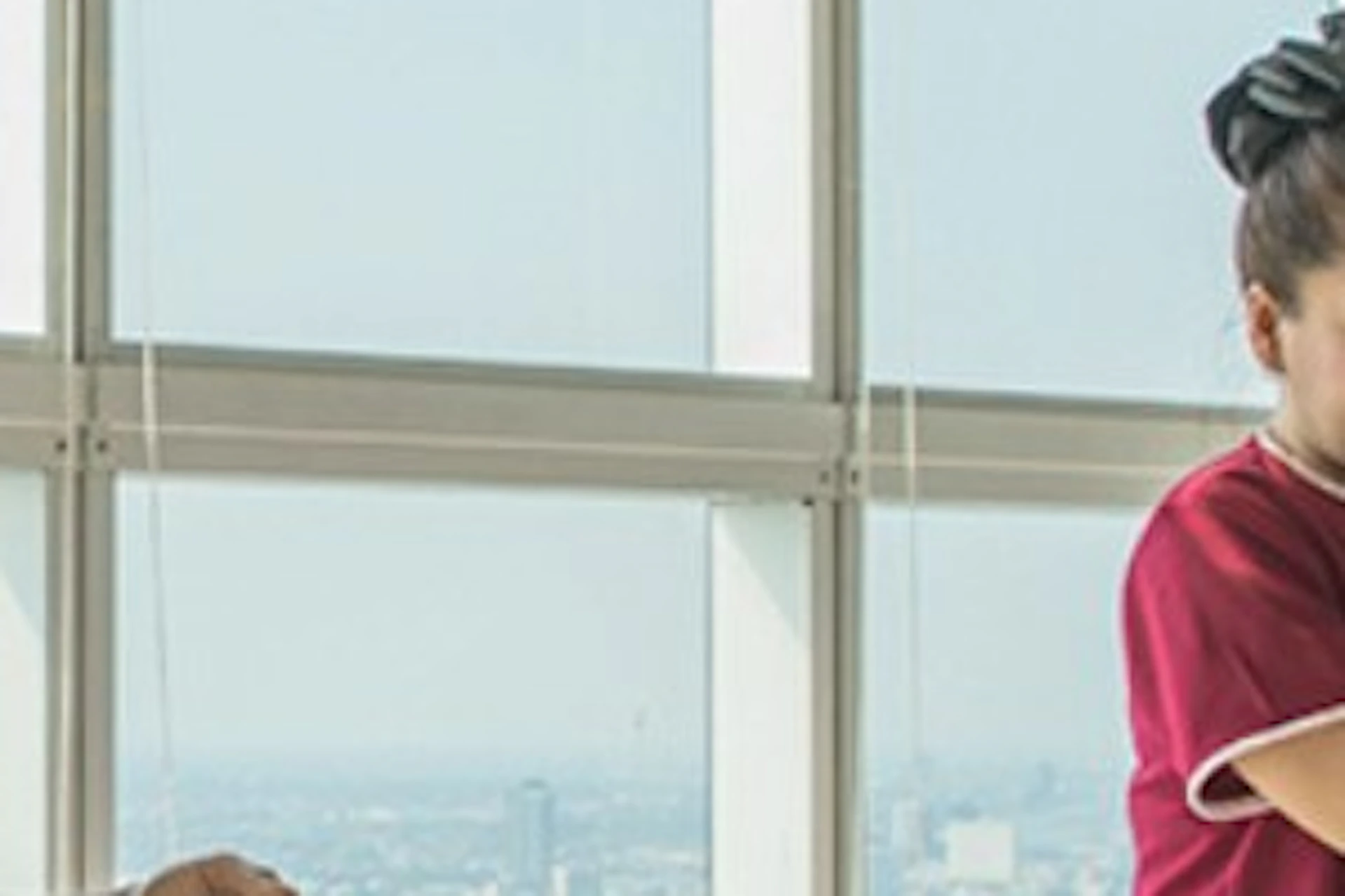Two massage therapists provide shoulder massages to clients sitting on mats in a bright room with large windows.