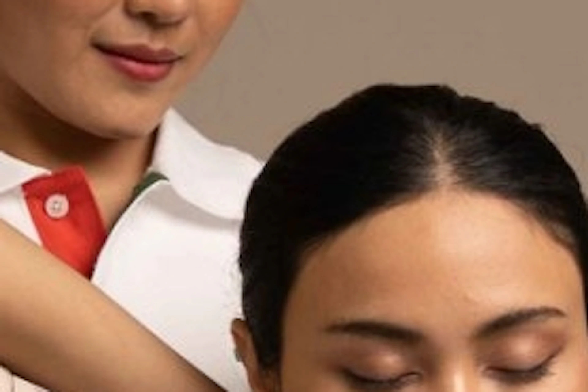 A person in uniform assists another sitting cross-legged in a beige outfit by stretching their arm in a calm setting.