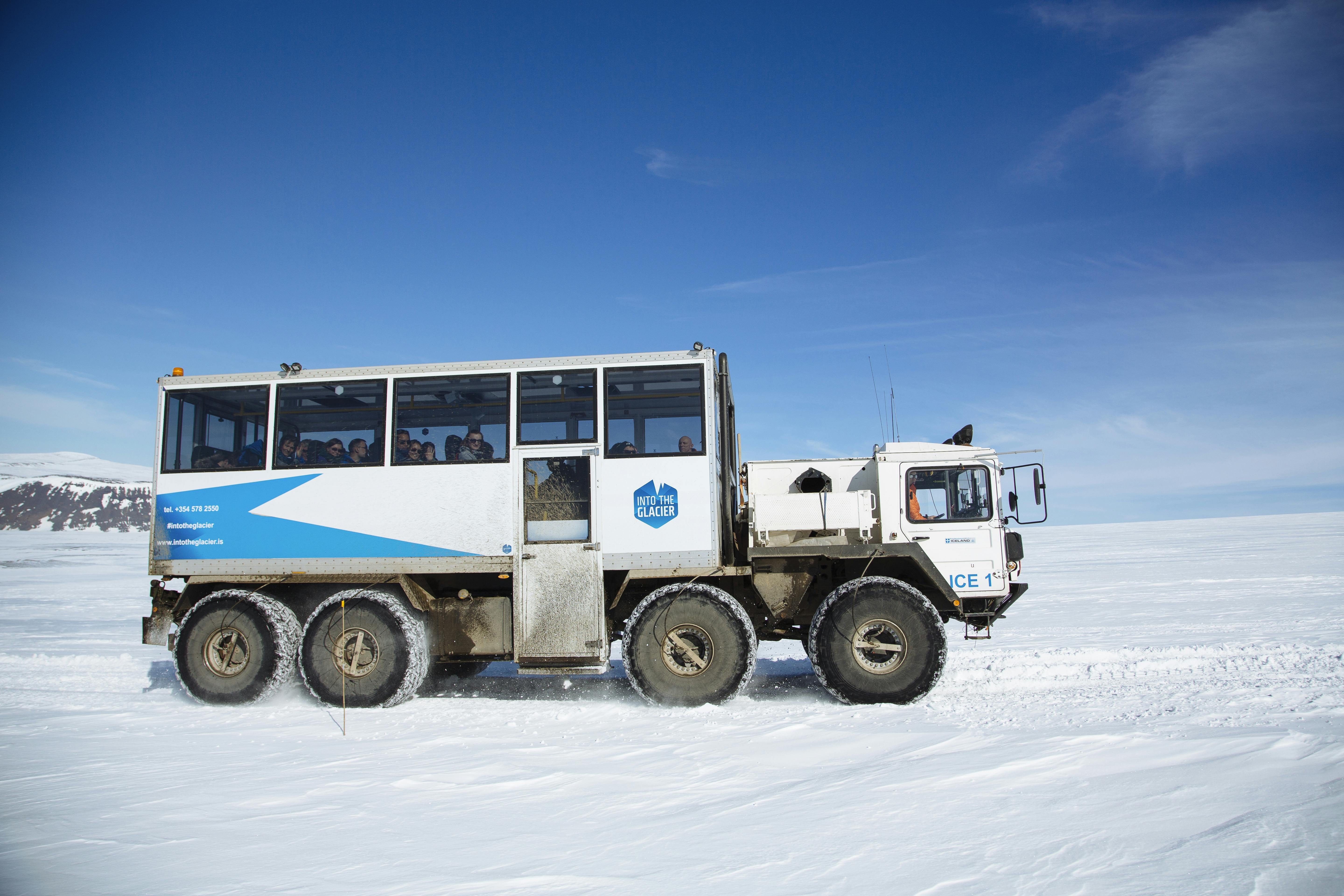 一辆带有“Into the Glacier”品牌的大型越野车在雪地上行驶，在晴朗的蓝天下载运乘客。