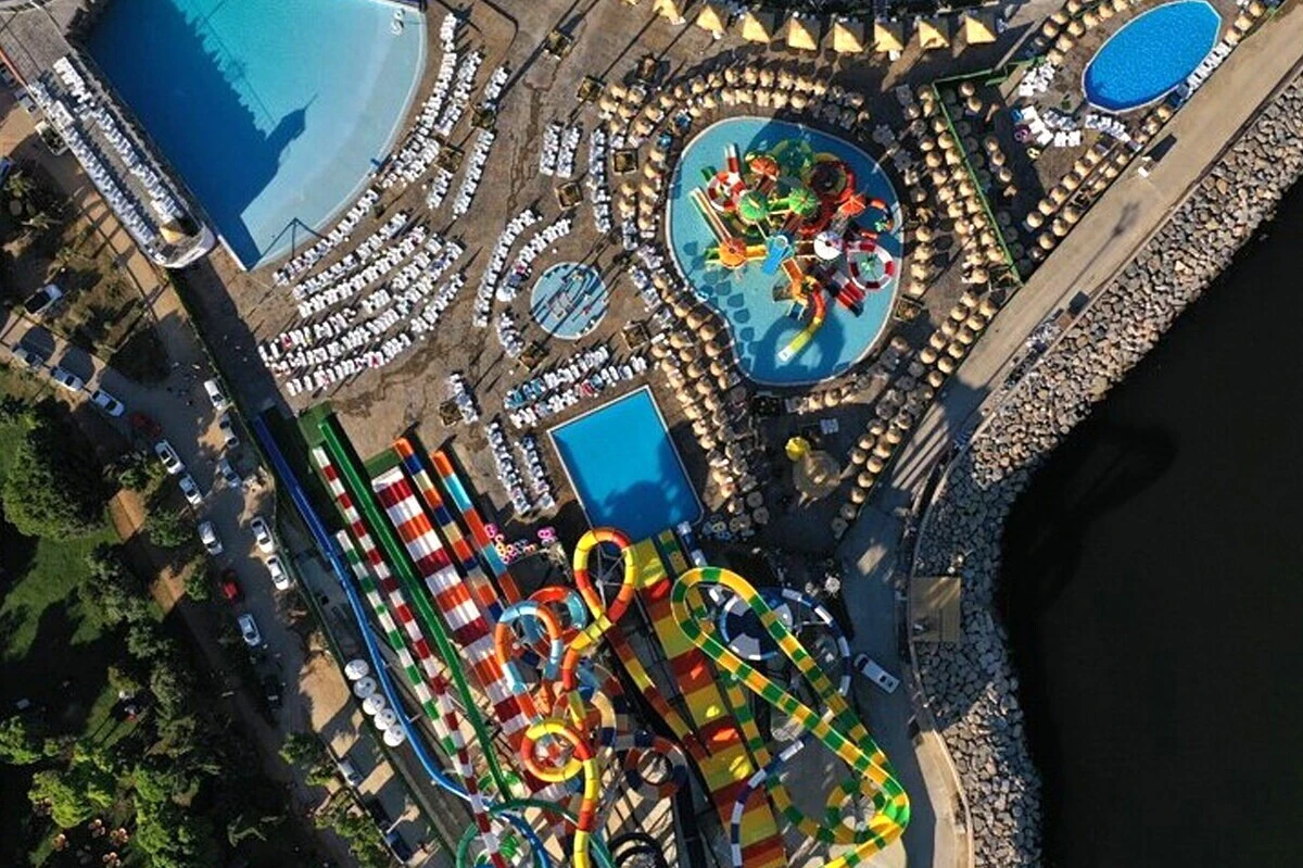 Aerial view of a waterpark with colorful slides, pools, sunshades, and lounge chairs arranged around the area.