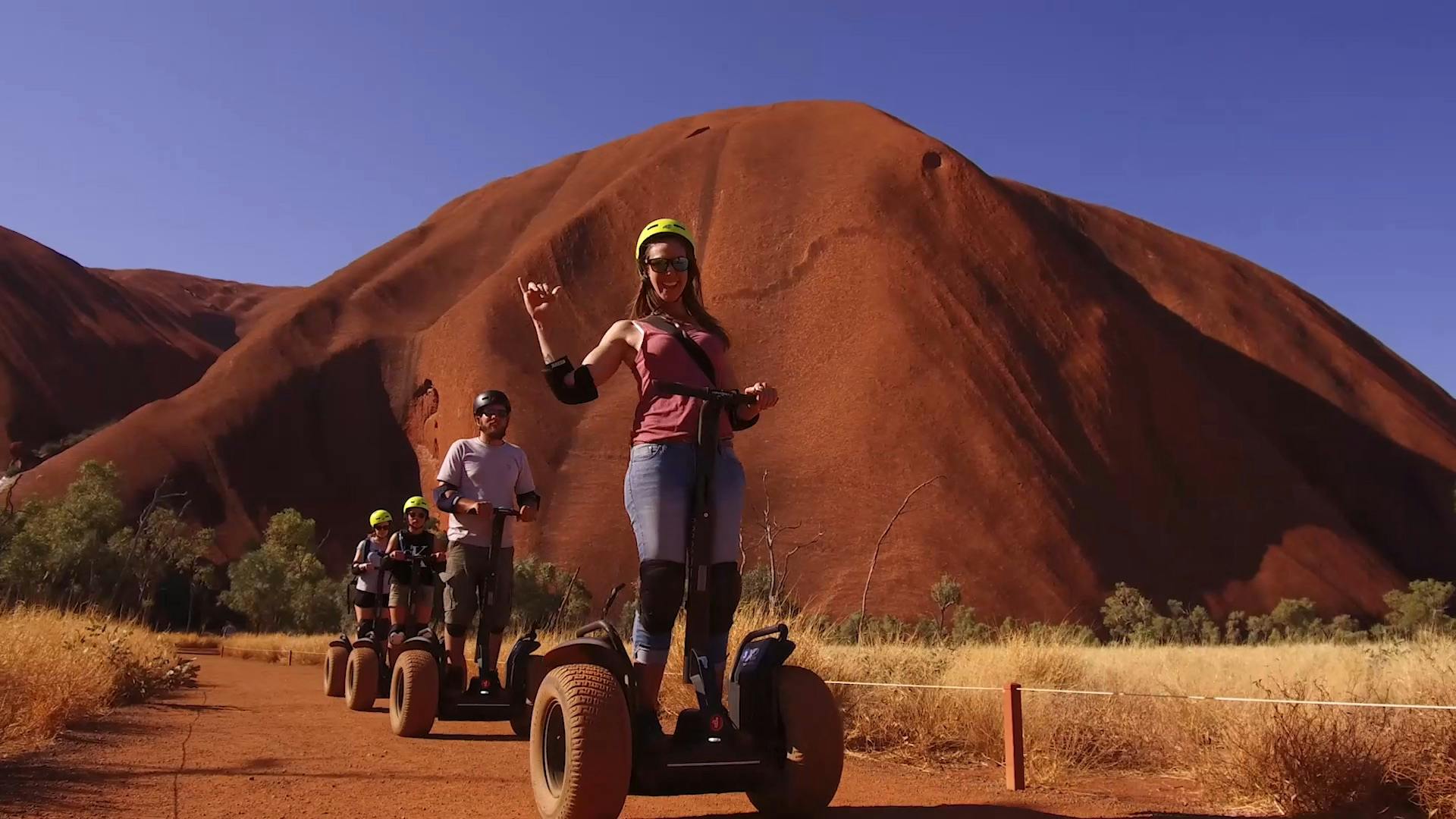 大きな赤い岩層を背景に、砂漠の風景の中でセグウェイに乗っている4人。