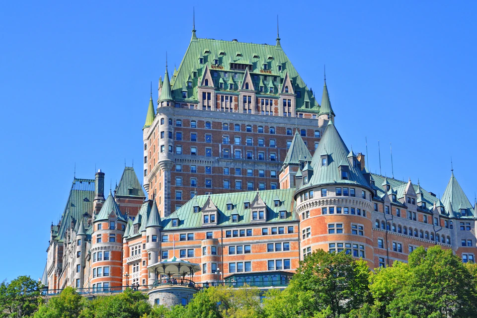 A historic building with green roofs and red brick walls under a clear blue sky, surrounded by trees.