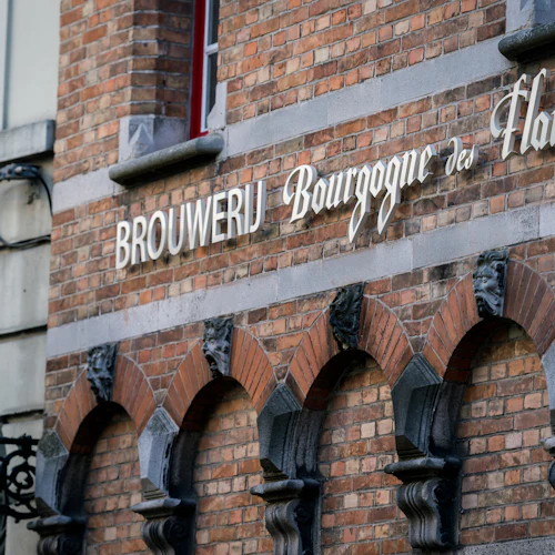 En tegelbyggnad med välvda fönster och en skylt med texten ”Brouwerij Bourgogne des Flandres”. En dekorativ lampa finns till vänster.