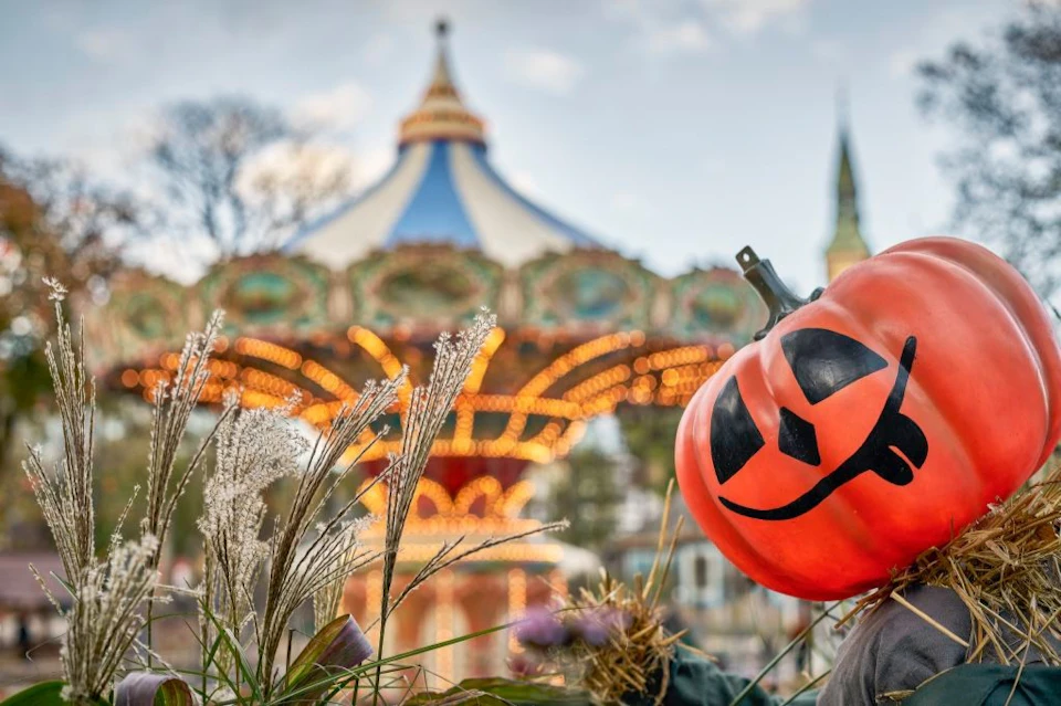 A glowing Jack-o'-lantern in front of a lit-up carousel with a blue and white top.