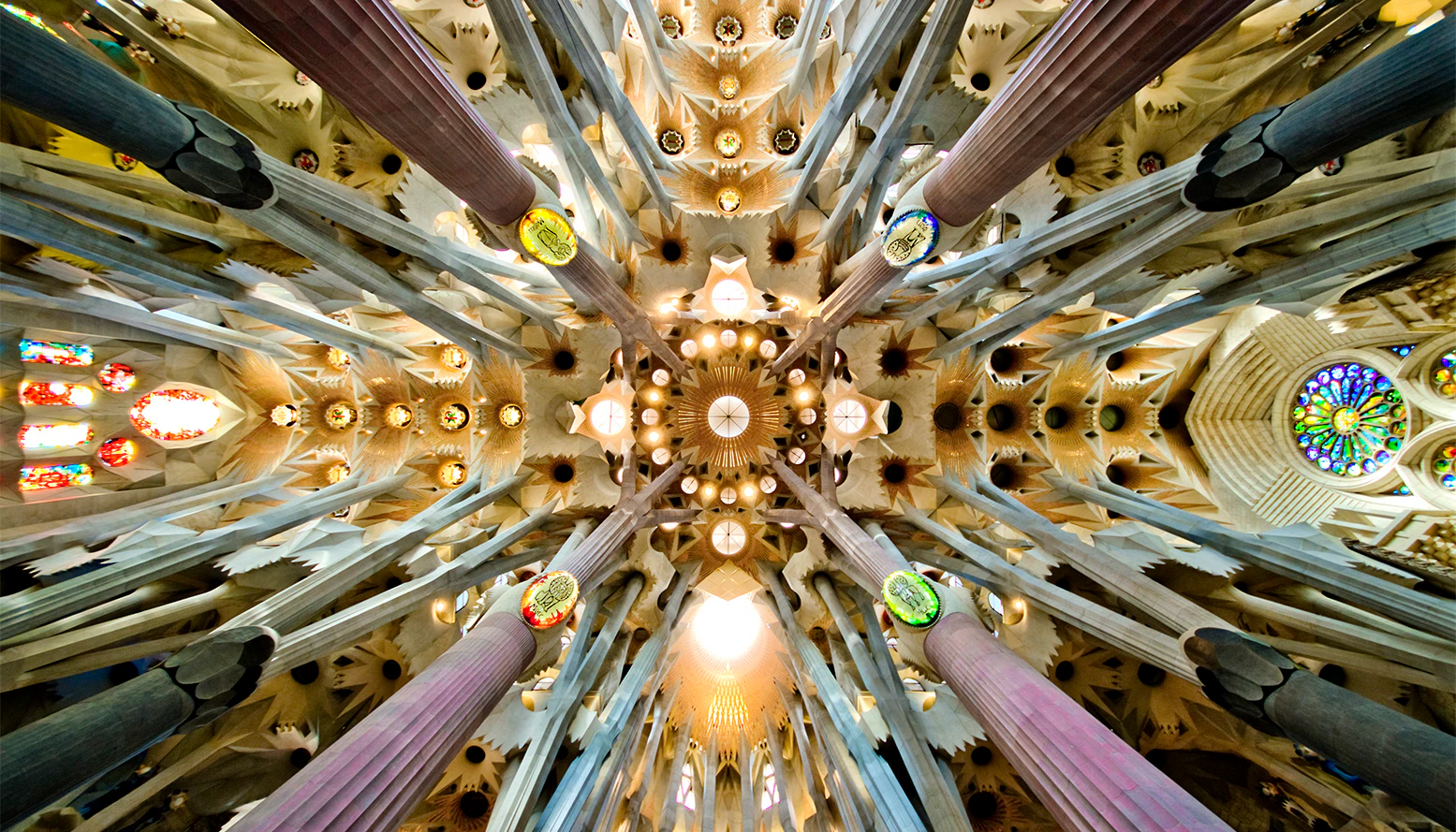 Ornate ceiling of a cathedral showcasing intricate patterns, decorative columns, and circular stained-glass windows.