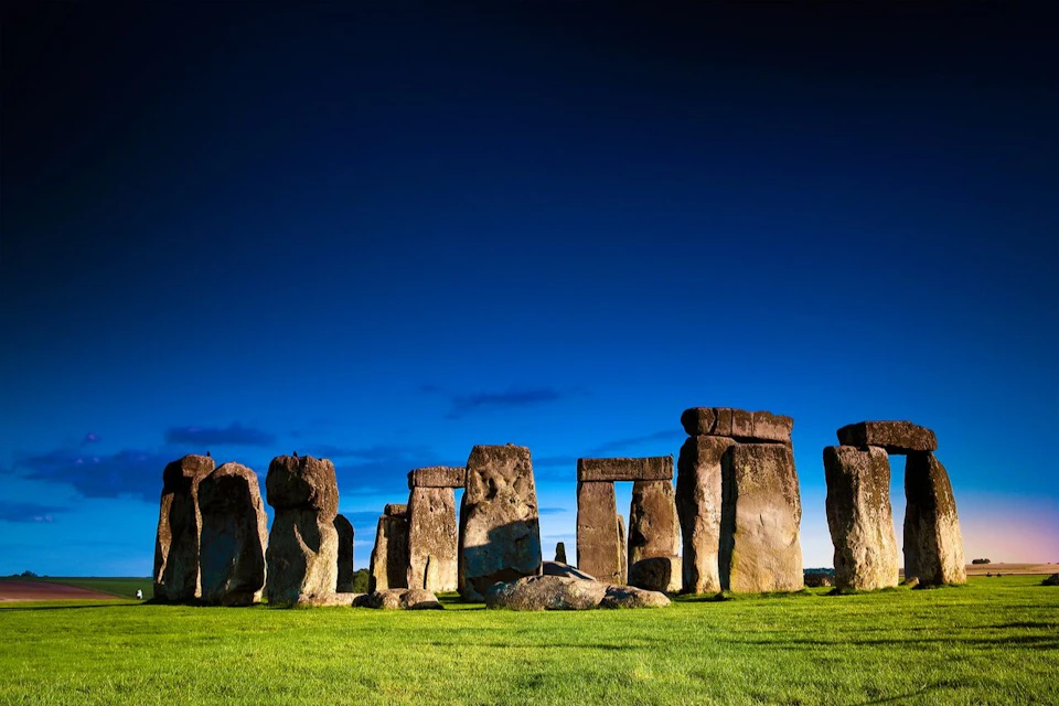 Stonehenge under a clear blue sky, with green grass in the foreground and the iconic stone arrangement in view.