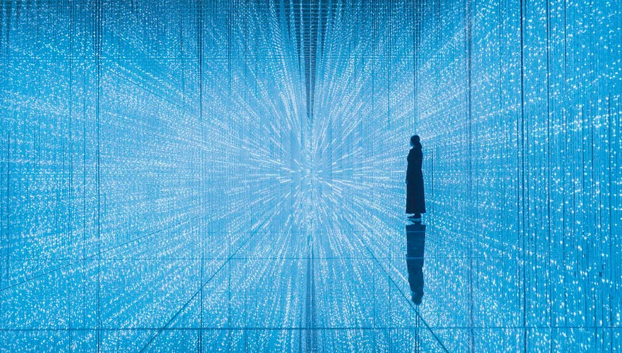 Una persona es troba enmig d'una habitació il·luminada i fascinant amb llums blaves que creen un efecte de patró infinit semblant a un túnel.