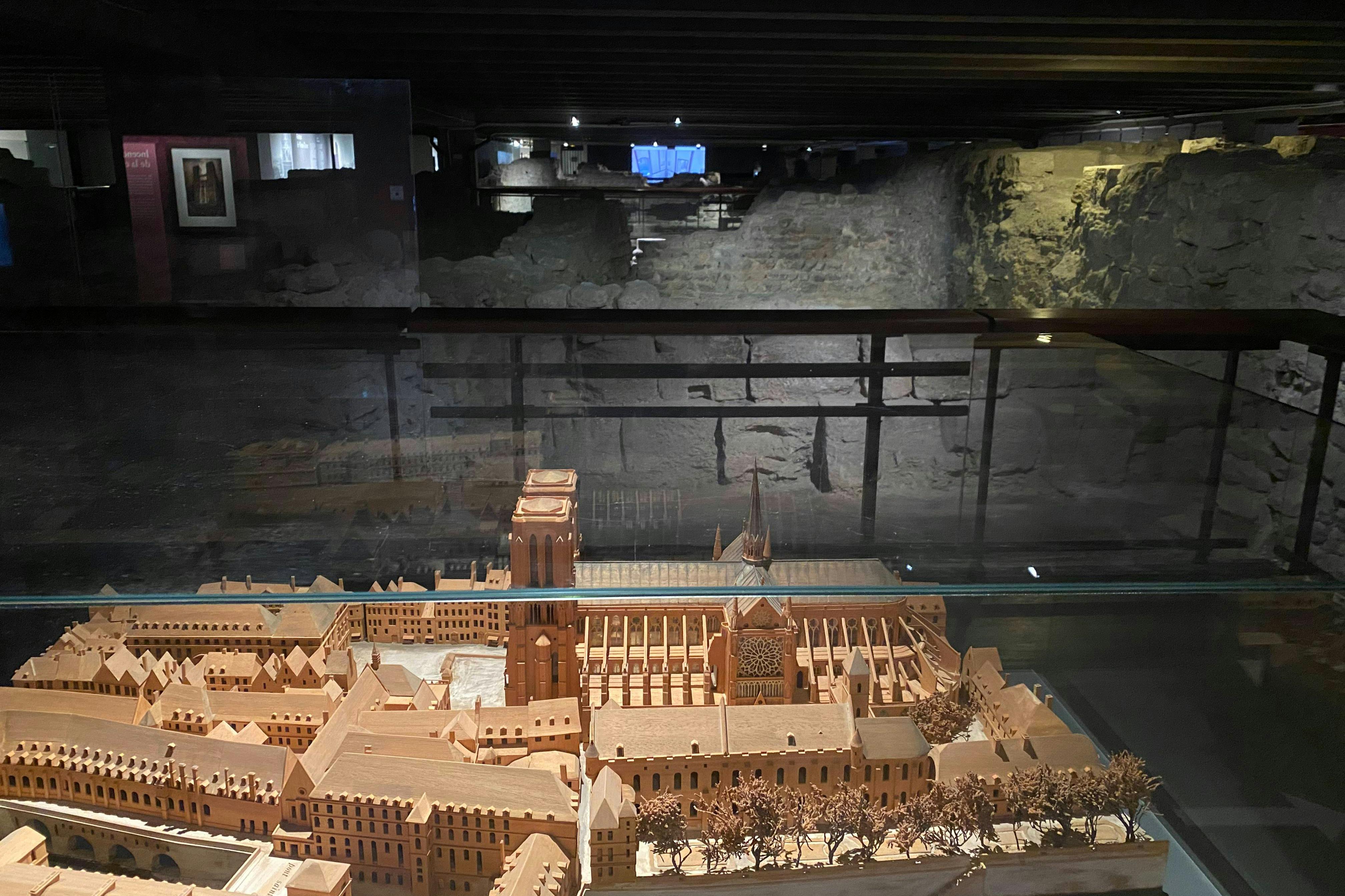 커다란 대성당이 있는 중세 도시의 상세한 목조 모델이 조명이 희미한 방의 유리 케이스에 전시되어 있습니다.