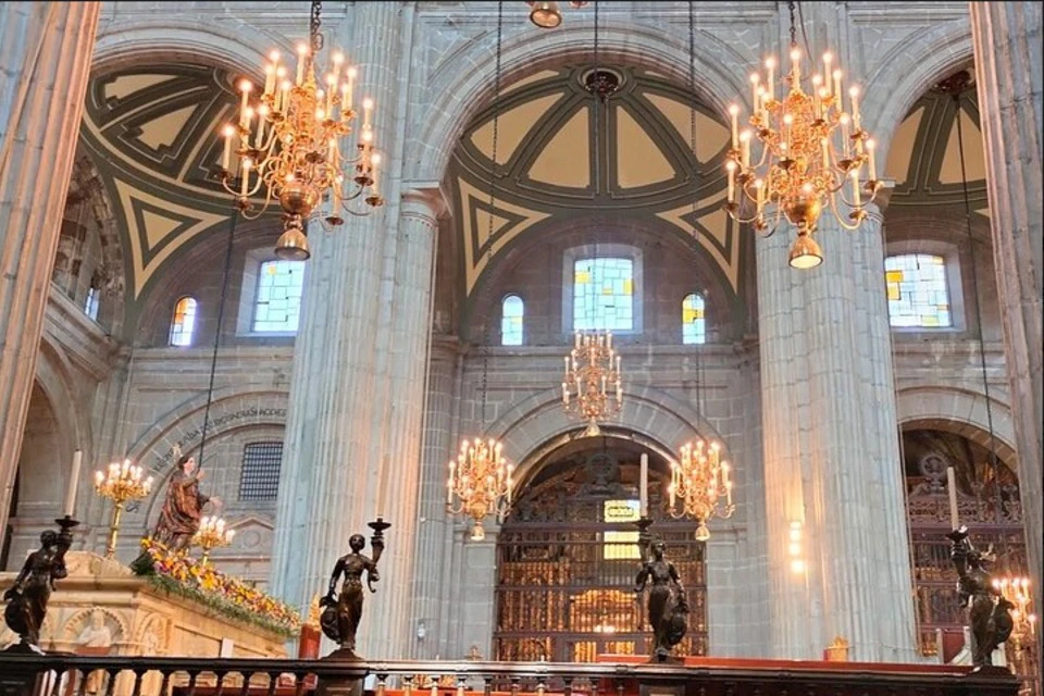 Interior of a grand cathedral with high arches, chandeliers, stained glass windows, and ornate statues.