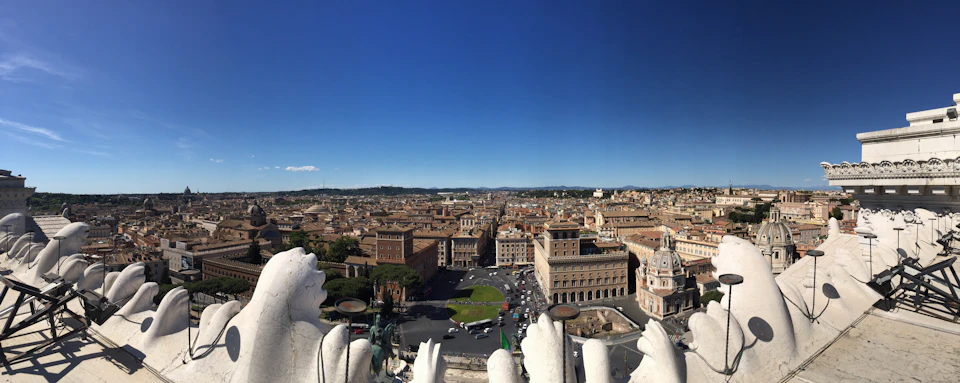 Aerial view of a city with historical architecture, a square with a circular green area, and multiple buildings under a clear blue sky.