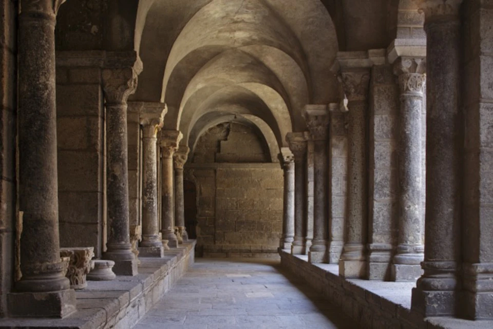 A stone hallway with arched ceilings, supported by columns, in what appears to be an ancient or historic building.