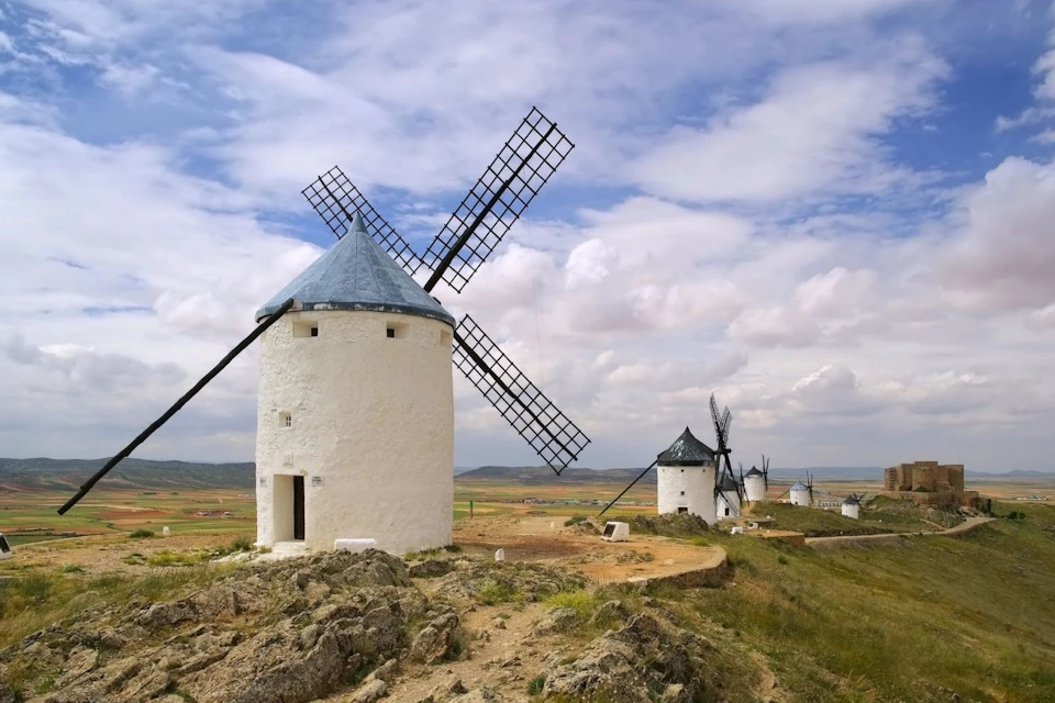 A row of traditional white windmills with black roofs on a hill under a partly cloudy sky.
