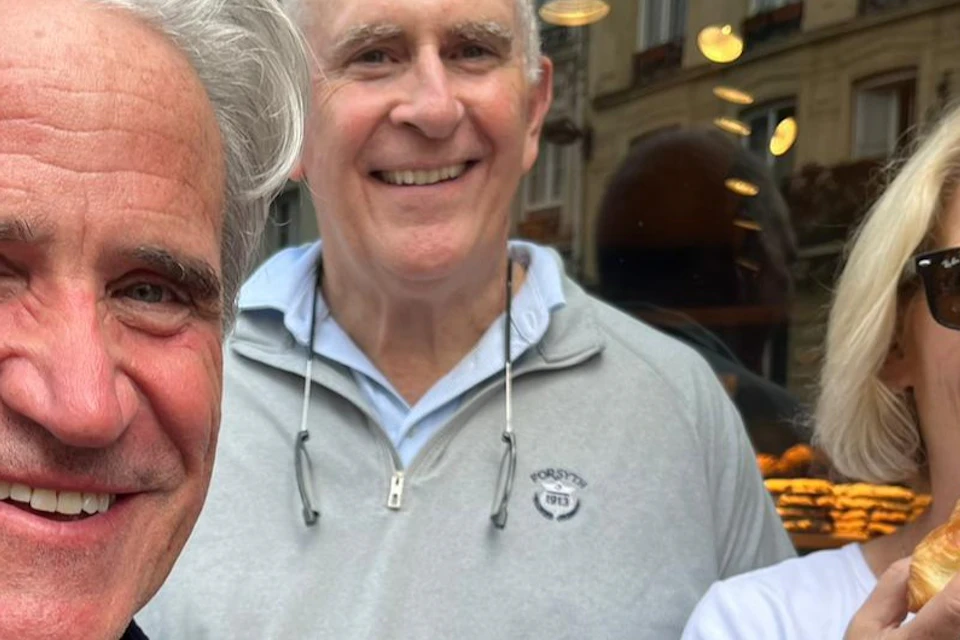 Three people smiling and holding croissants in front of a bakery.