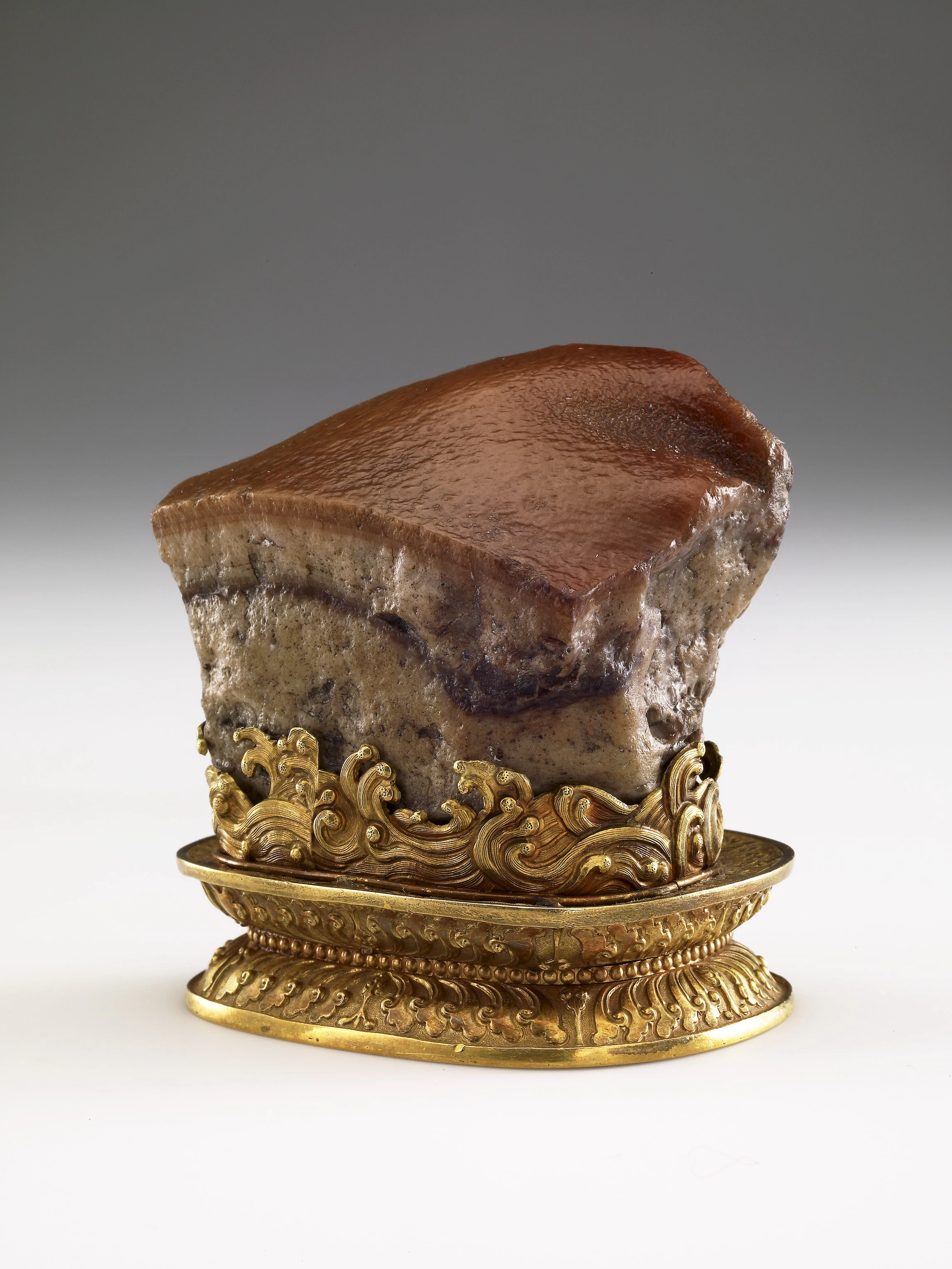 A carved stone with a brown top displayed on an ornate gold stand with intricate details.