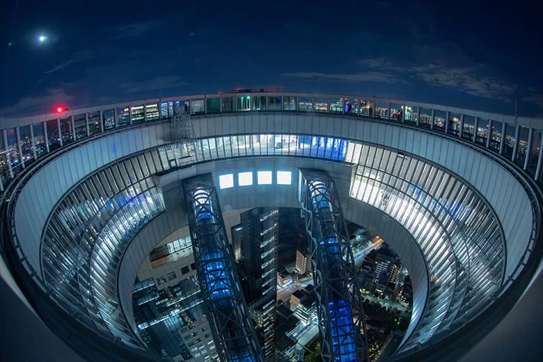 A circular rooftop observation deck with illuminated walkways, overlooking a cityscape at night.