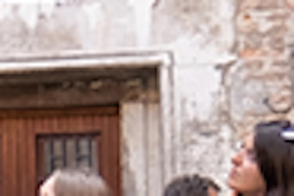 A tour guide gestures while speaking to a group of people in front of a historic building labeled "CASA DI MARCO POLO."
