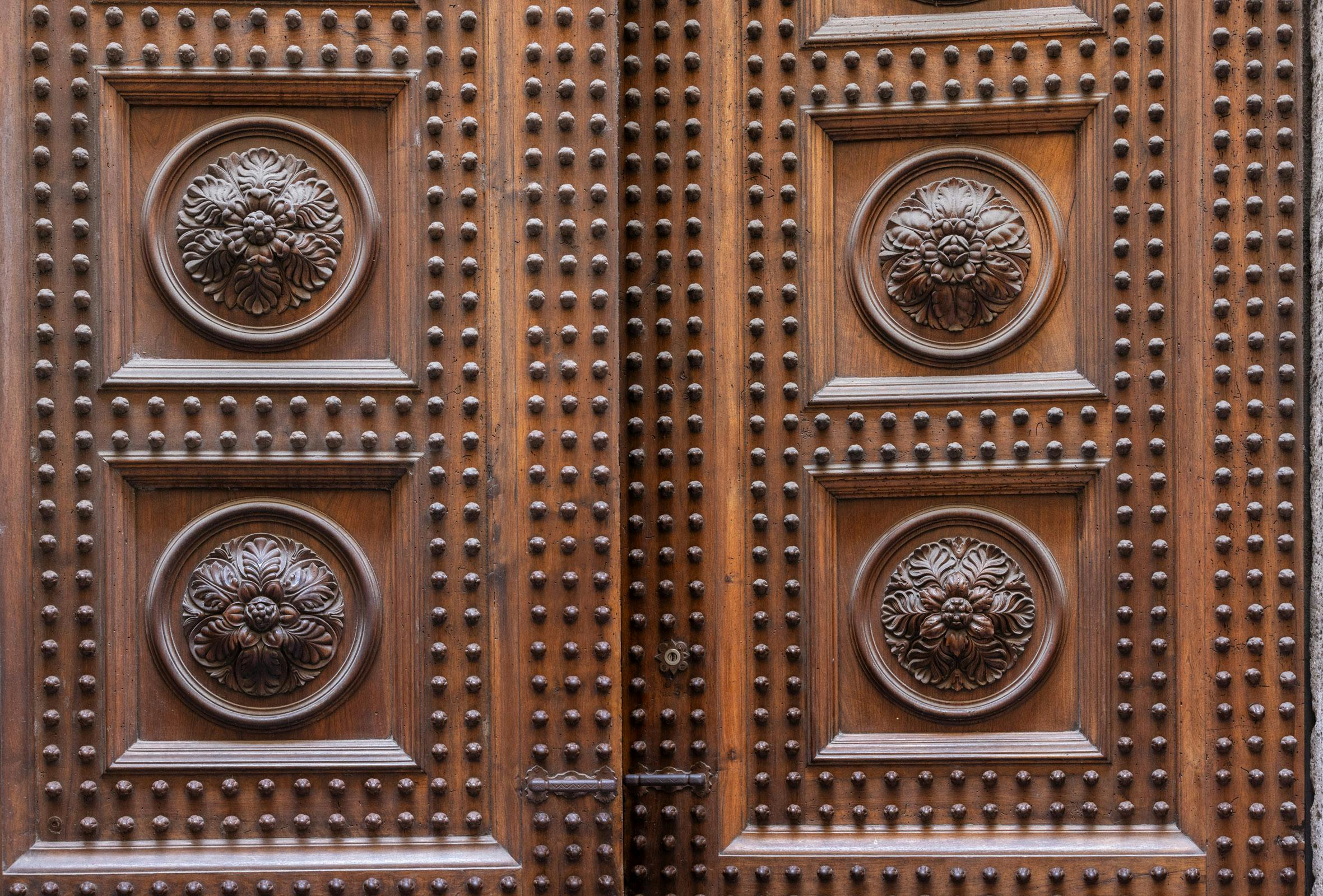 Primo piano di una porta di legno ornata con intricati intagli e motivi floreali decorativi rotondi, costellati da numerosi rivetti.