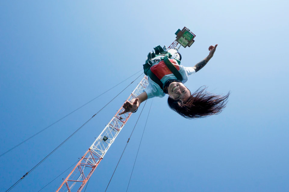 A person bungee jumping from a tall crane, smiling against a clear blue sky.