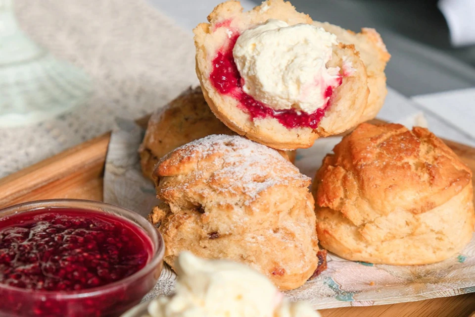 Freshly baked scones with jam, clotted cream, and a bowl of raspberry jam on the side.