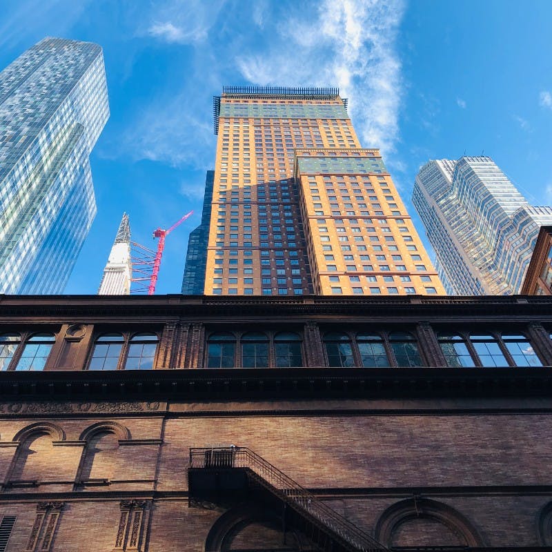 Ψηλά κτίρια κάτω από έναν καταγάλανο ουρανό, με παλαιότερο κτίριο από τούβλα σε πρώτο πλάνο και έναν κόκκινο γερανό ανάμεσα στους ουρανοξύστες.