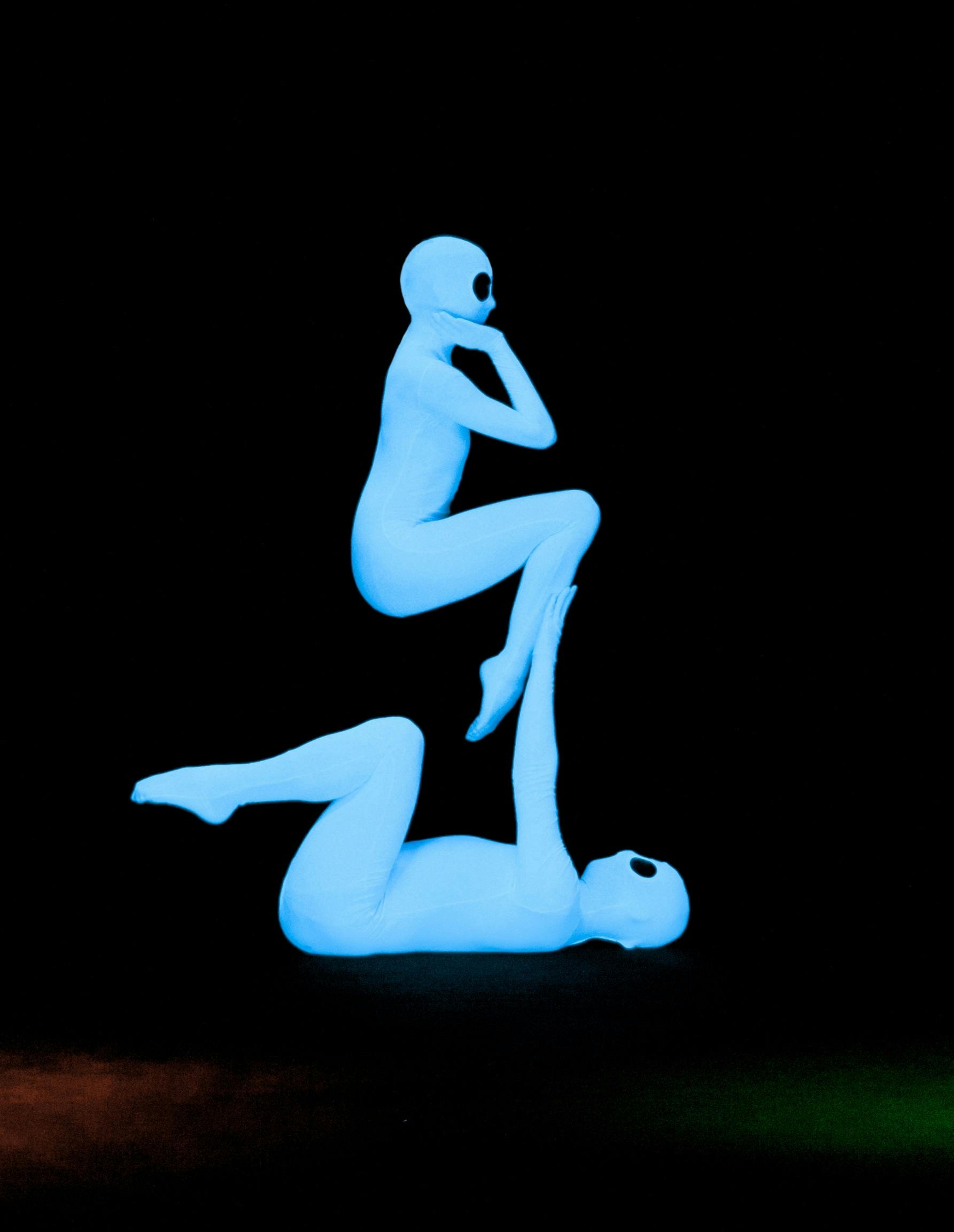 Two glowing blue humanoid figures with large eyes performing an acrobatic pose against a black background.