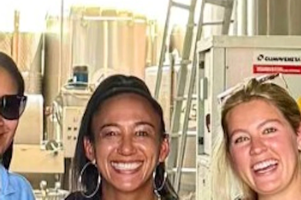 Five people standing together smiling in an industrial facility with large tanks and bright lighting in the background.