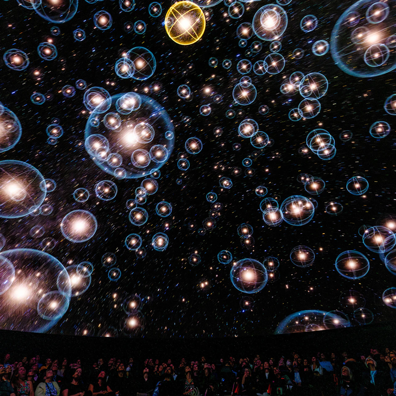 A planetarium show featuring a starry sky with bubble-like visuals projected on the dome above an audience.