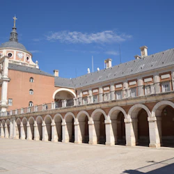En historisk byggnad med välvda gångar, ett klocktorn och en kupol under en klarblå himmel.