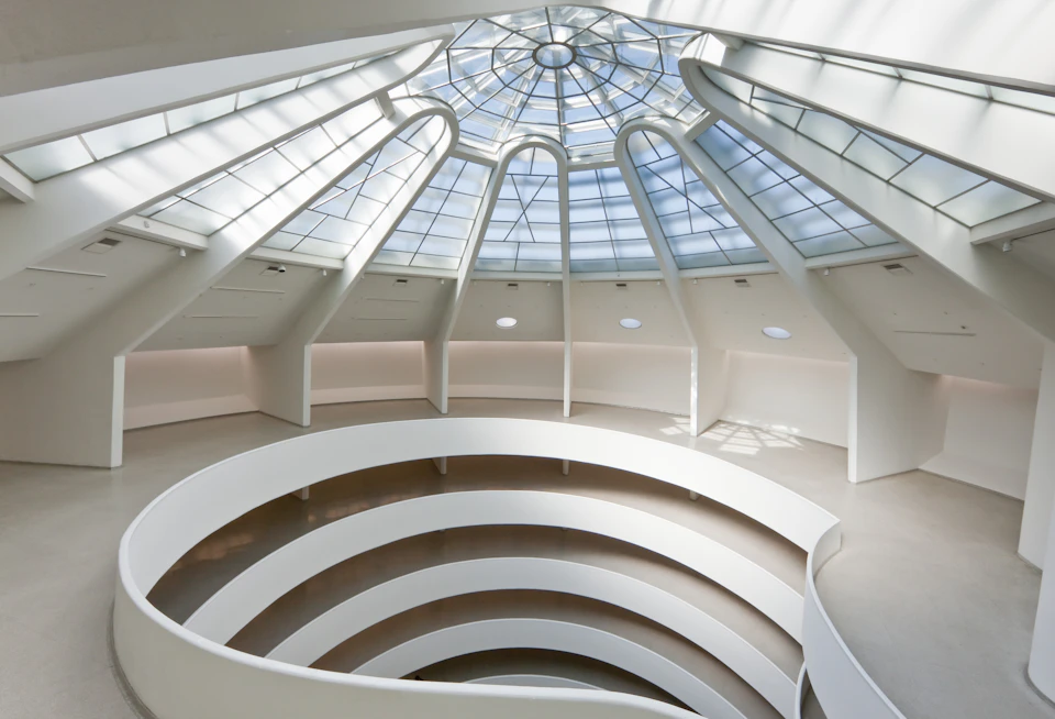 A spacious, modern atrium with a large glass-domed ceiling and a spiraling, circular walkway below.