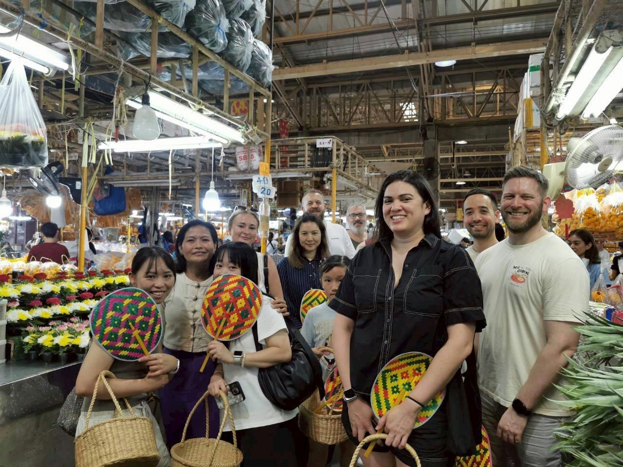 A group of people smiling and holding baskets in a market with colorful goods and a high ceiling.
