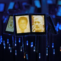 Två upplysta porträttskärmar bland många, med en leende kvinna och en skäggig man mot en bakgrund av blått ljus.