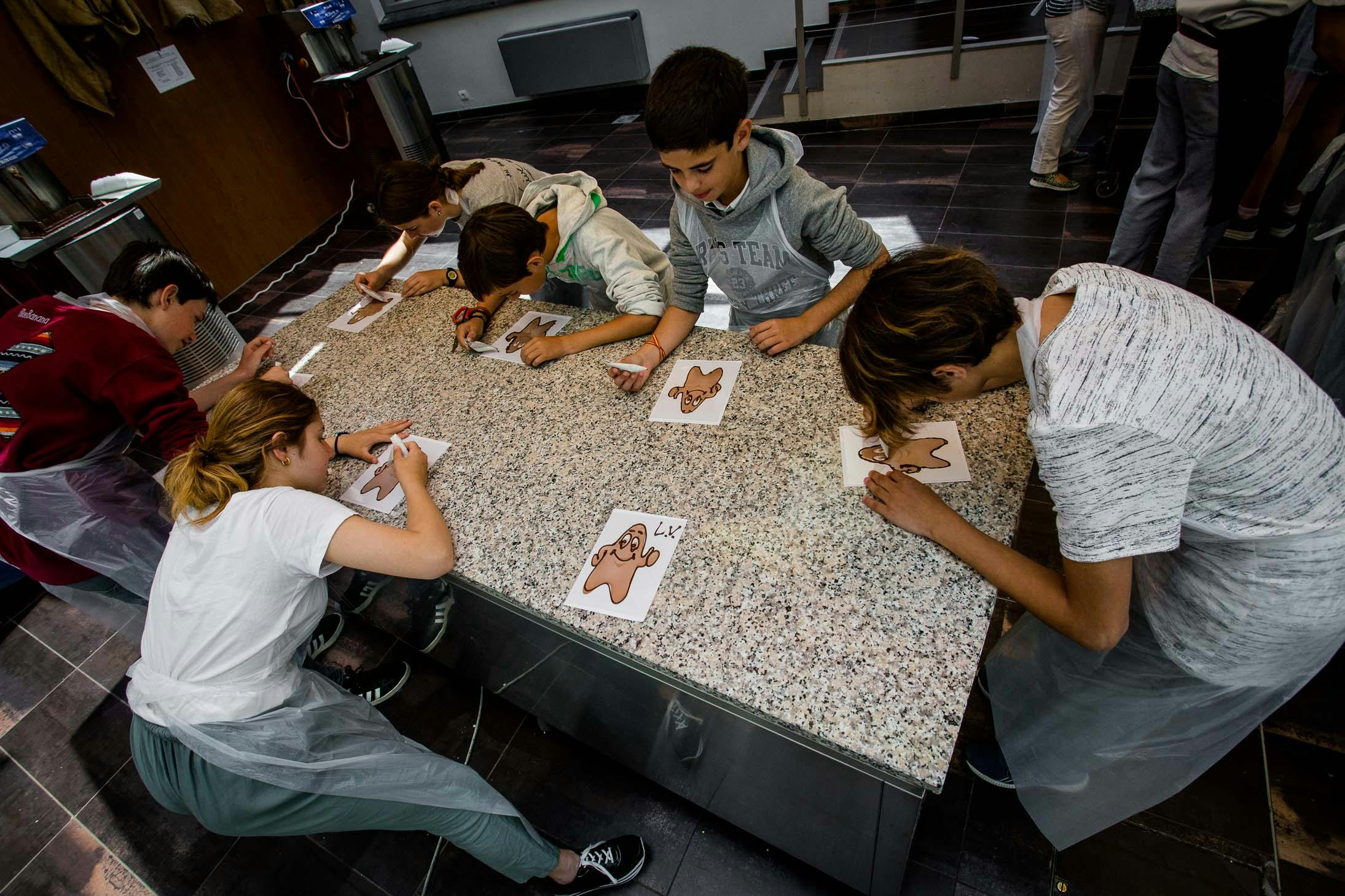 一群孩子在厨房柜台上用糖霜装饰姜饼人，他们都专注于各自的饼干。