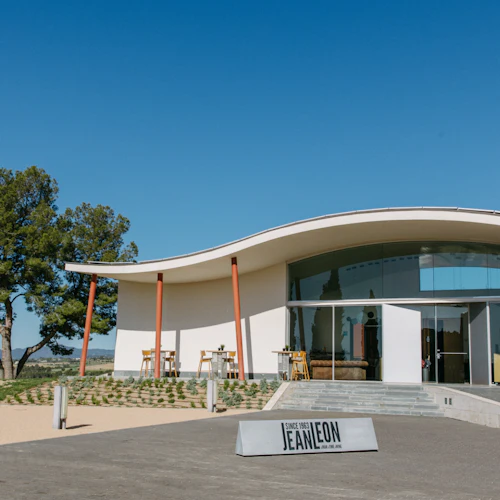 Modern byggnad med böjt tak, stora glasfönster och lite uteservering. Träd finns i bakgrunden. På skylten står det "Jean Leon".
