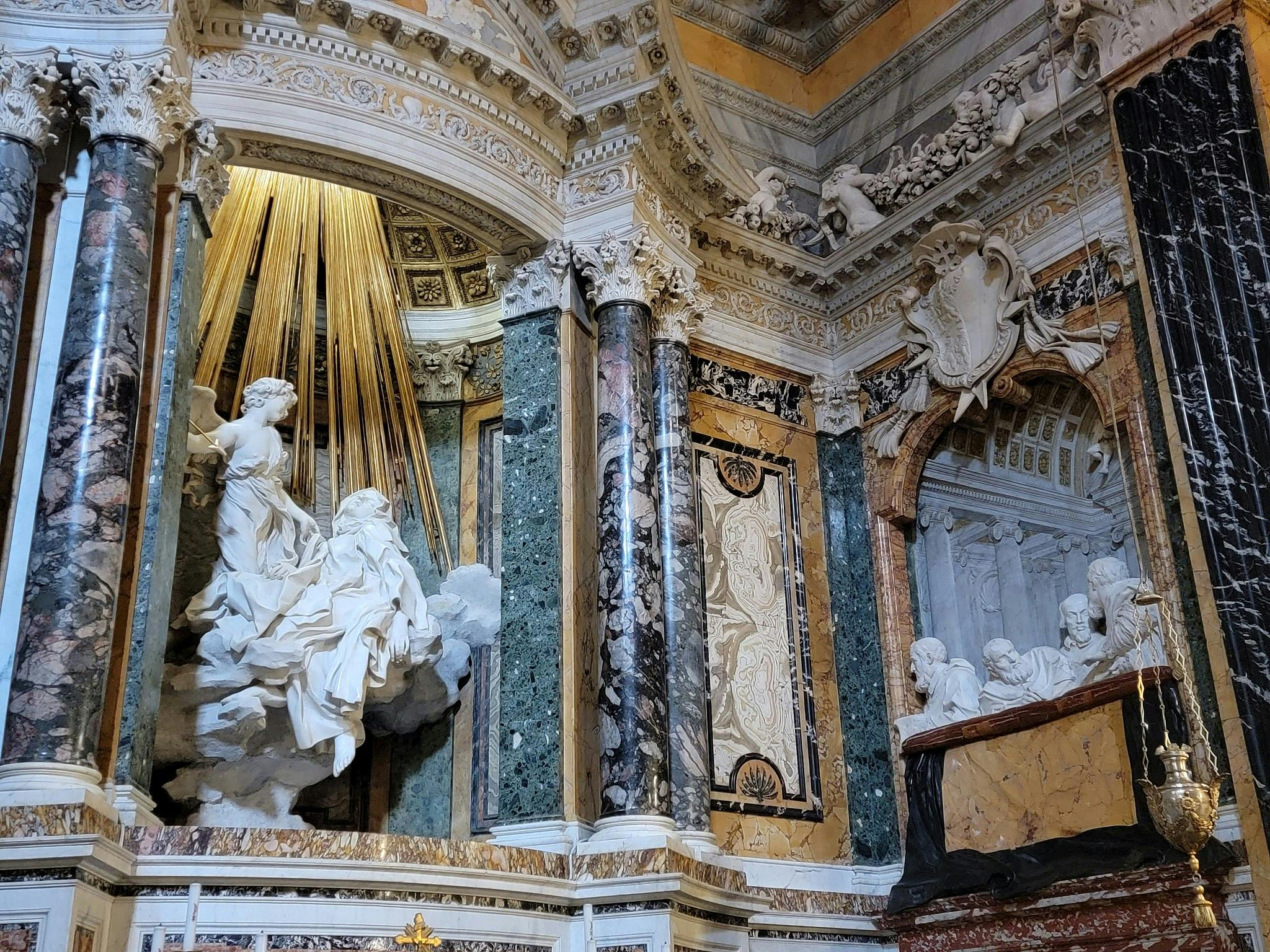 Udsmykket barok interiør med marmorsøjler, indviklede udskæringer og statuer, herunder en central figur omgivet af gyldne stråler.