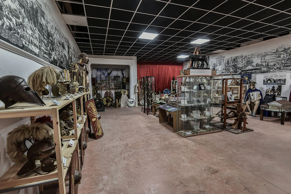Room filled with historical artifacts, including helmets, shields, glass display cases, and murals on the walls.